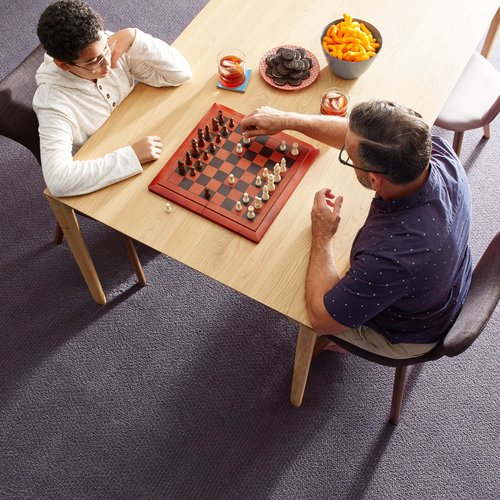 People playing chess at a wooden table in a room with purple carpet from Success Floor Covering LLC in Oakland, MD